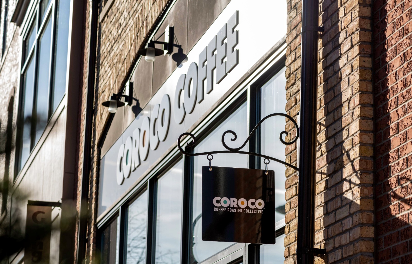Exterior view of Coroco Coffee storefront in downtown St. Charles with hanging logo sign and brick facade.